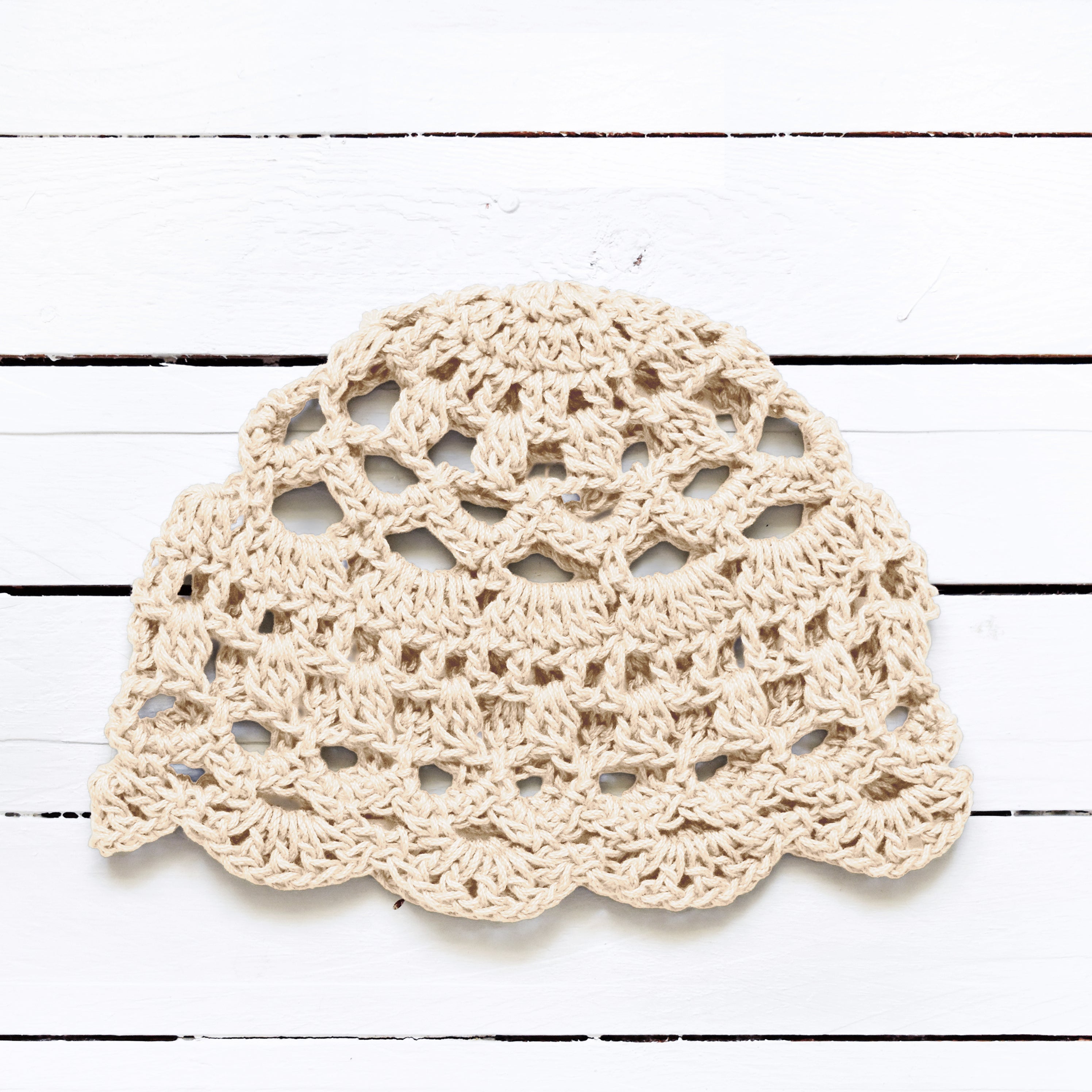 Beige crocheted skull cap on a white wooden surface.