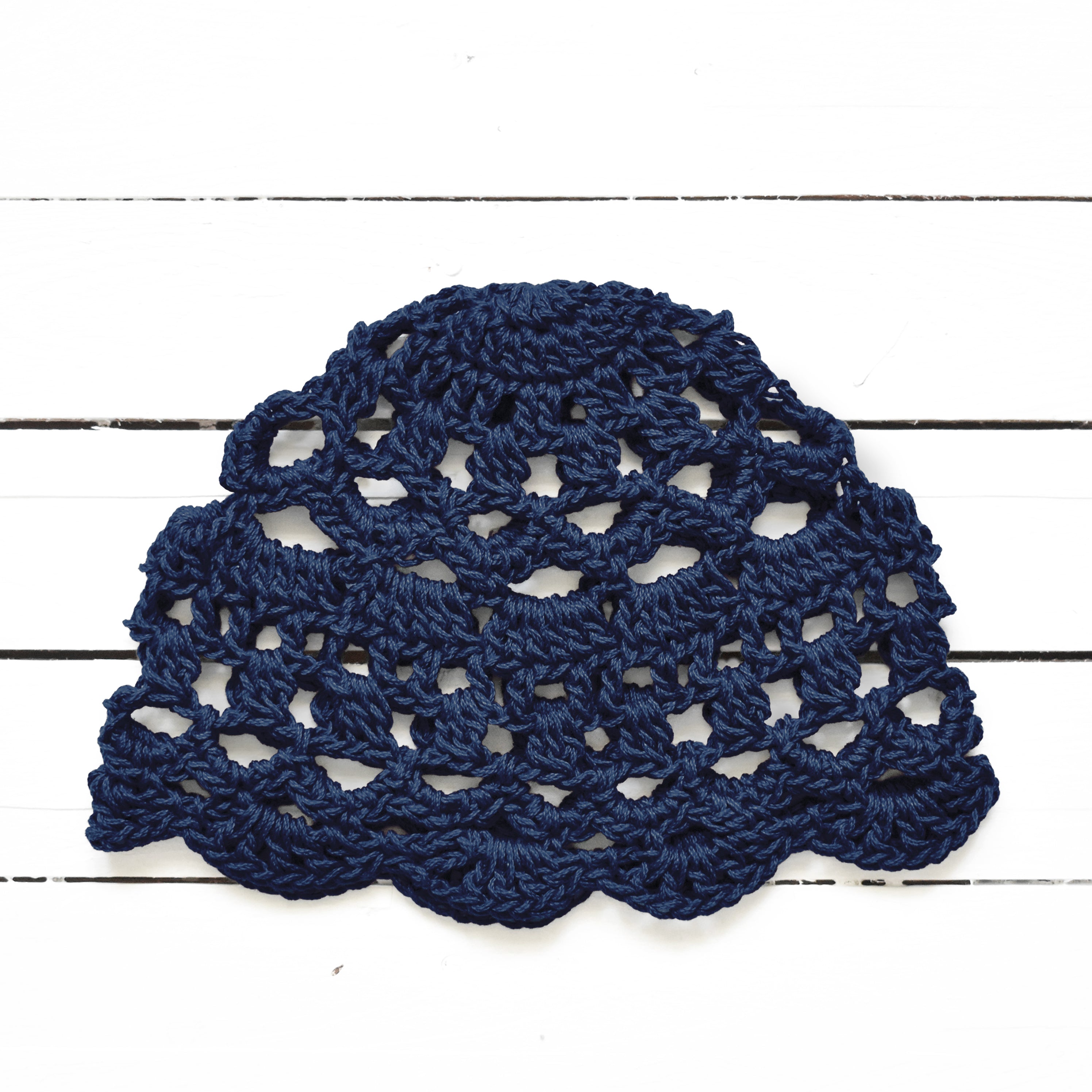 Navy blue crocheted summer cap on a white wooden surface.