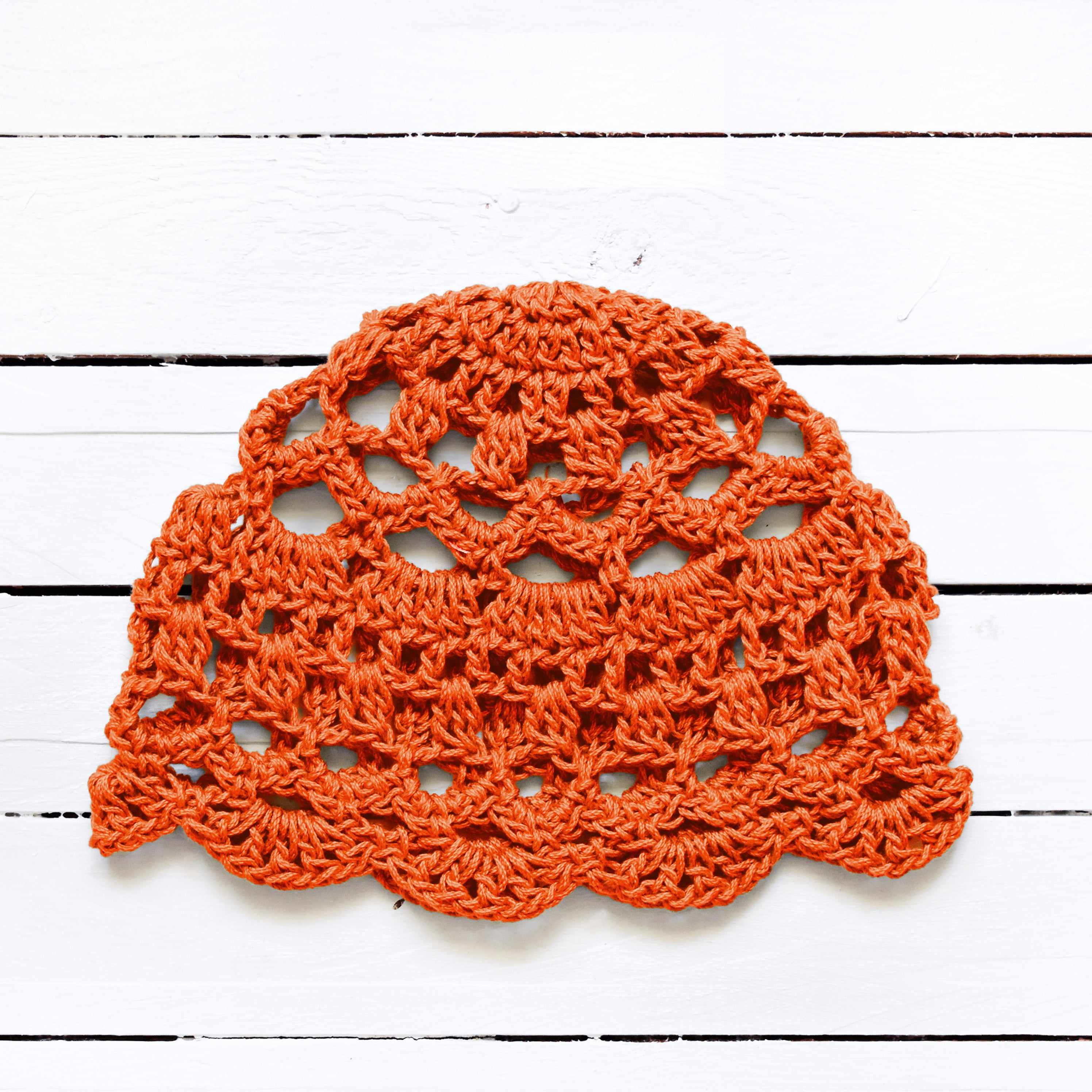Orange crocheted lace cap on a white wooden surface.