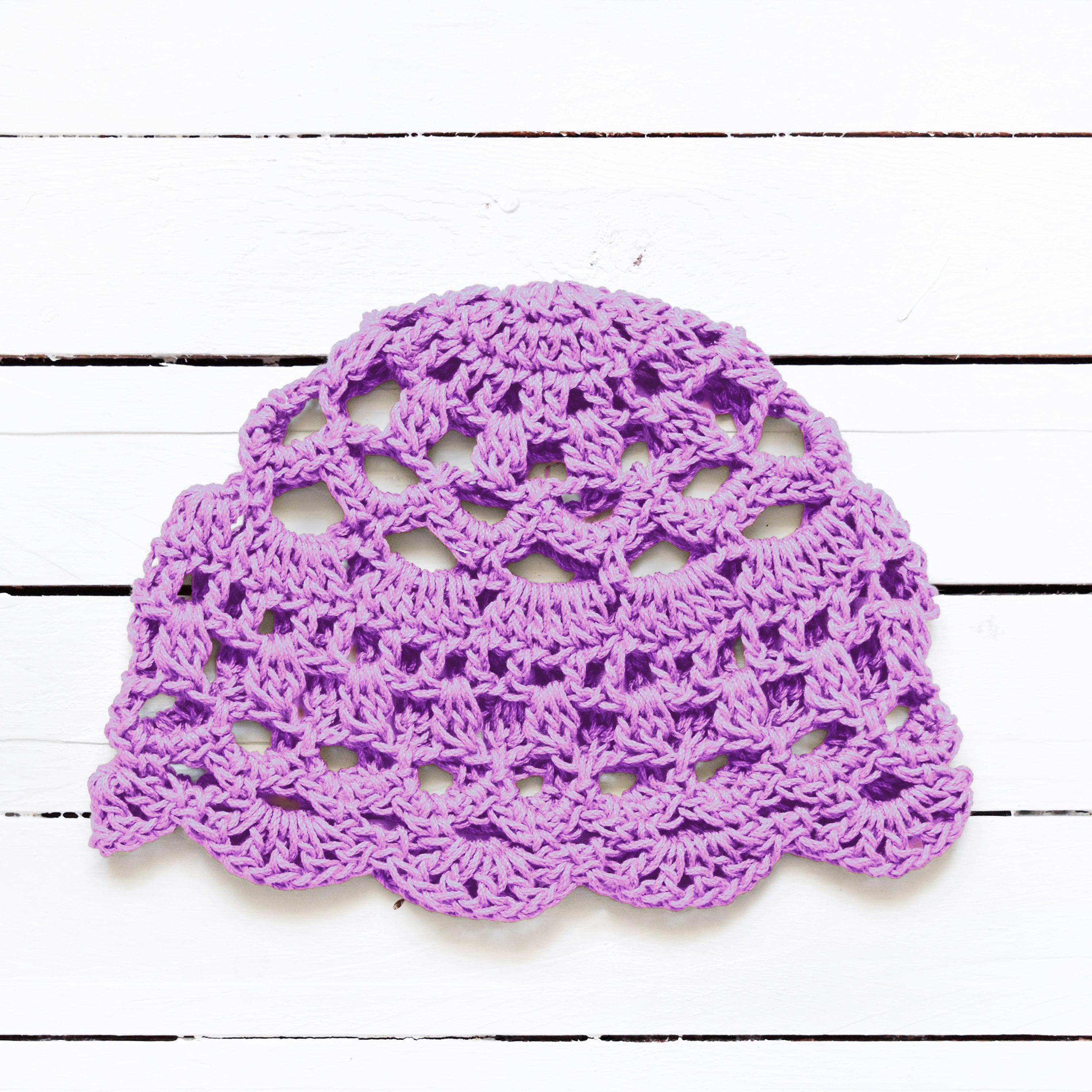 Light purple crocheted doily on a white wooden surface.