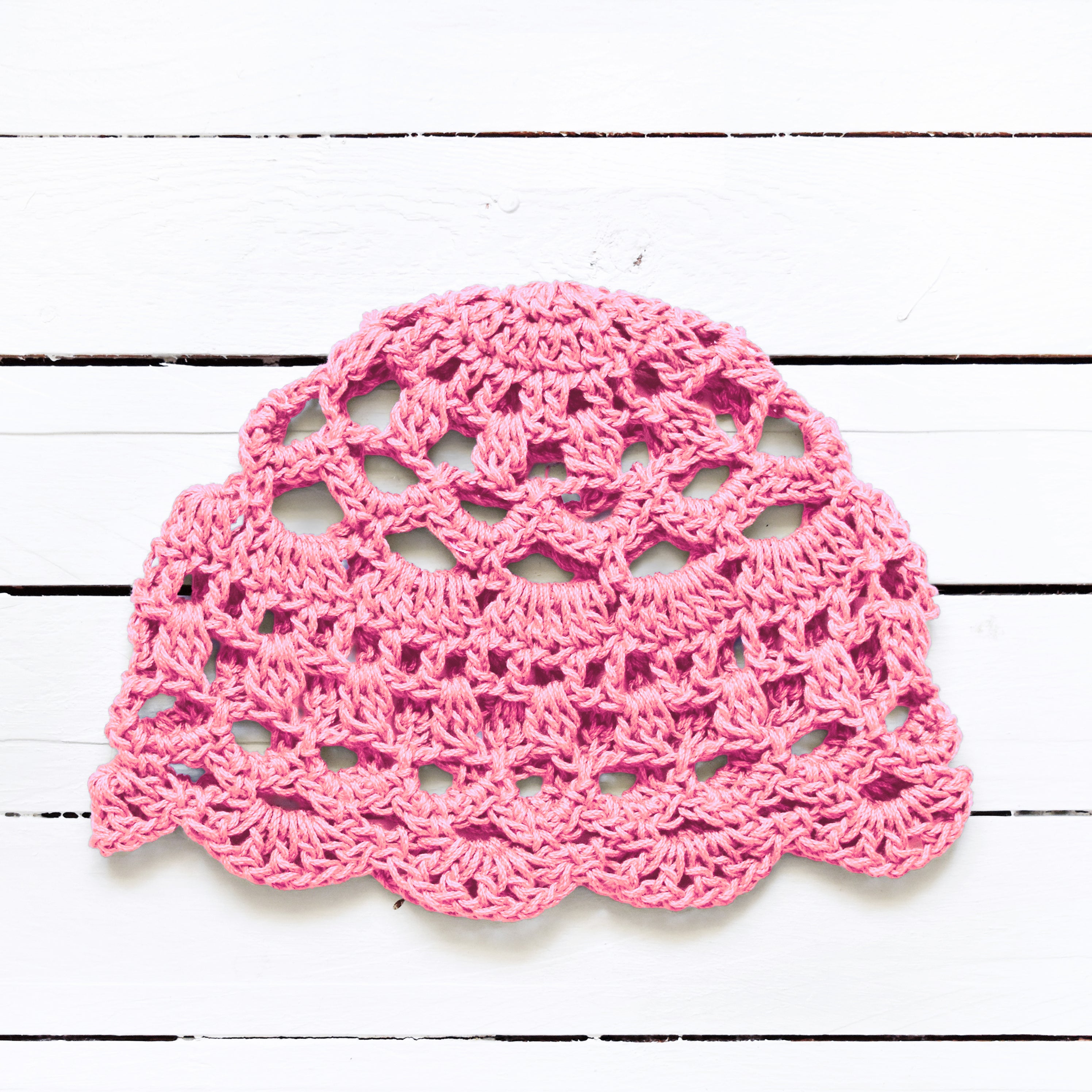 Pink crocheted boho lace cap on a white wooden surface.