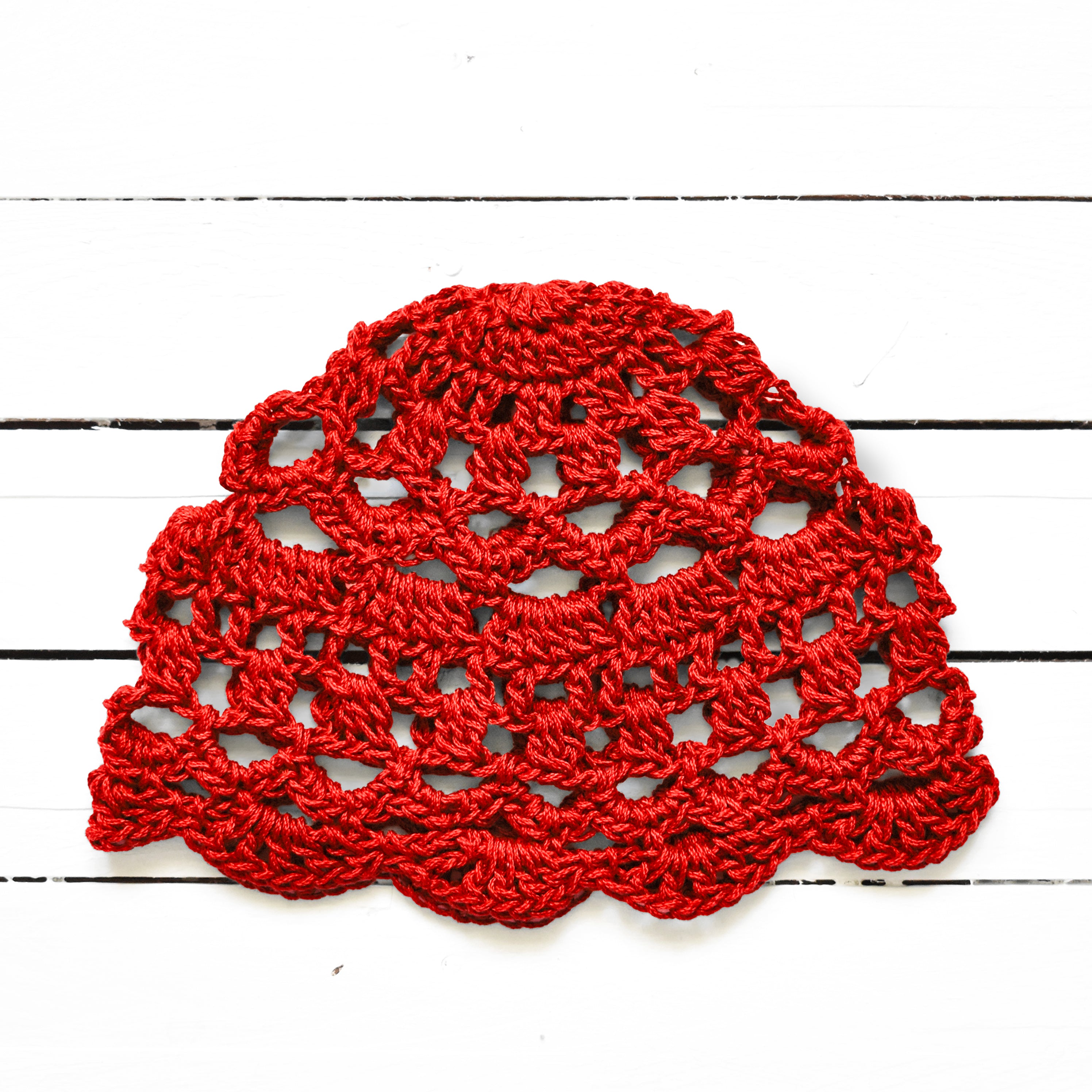 Red crocheted boho lace cap on a white wooden surface.