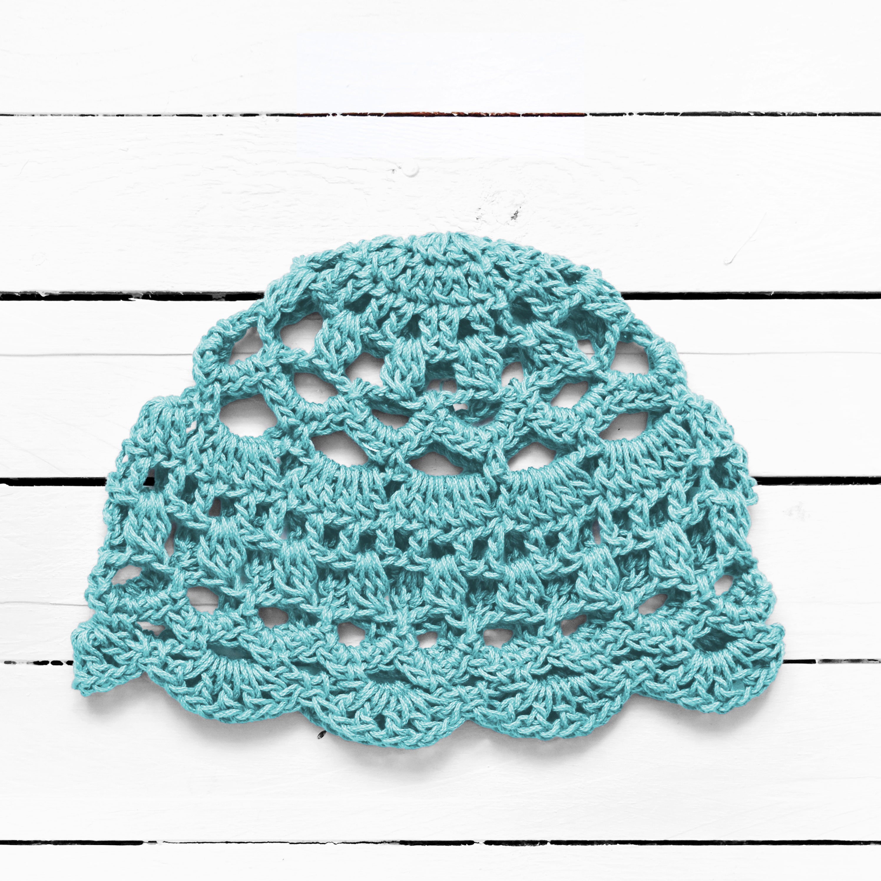 Light blue bohemian crocheted cap on a white wooden surface.