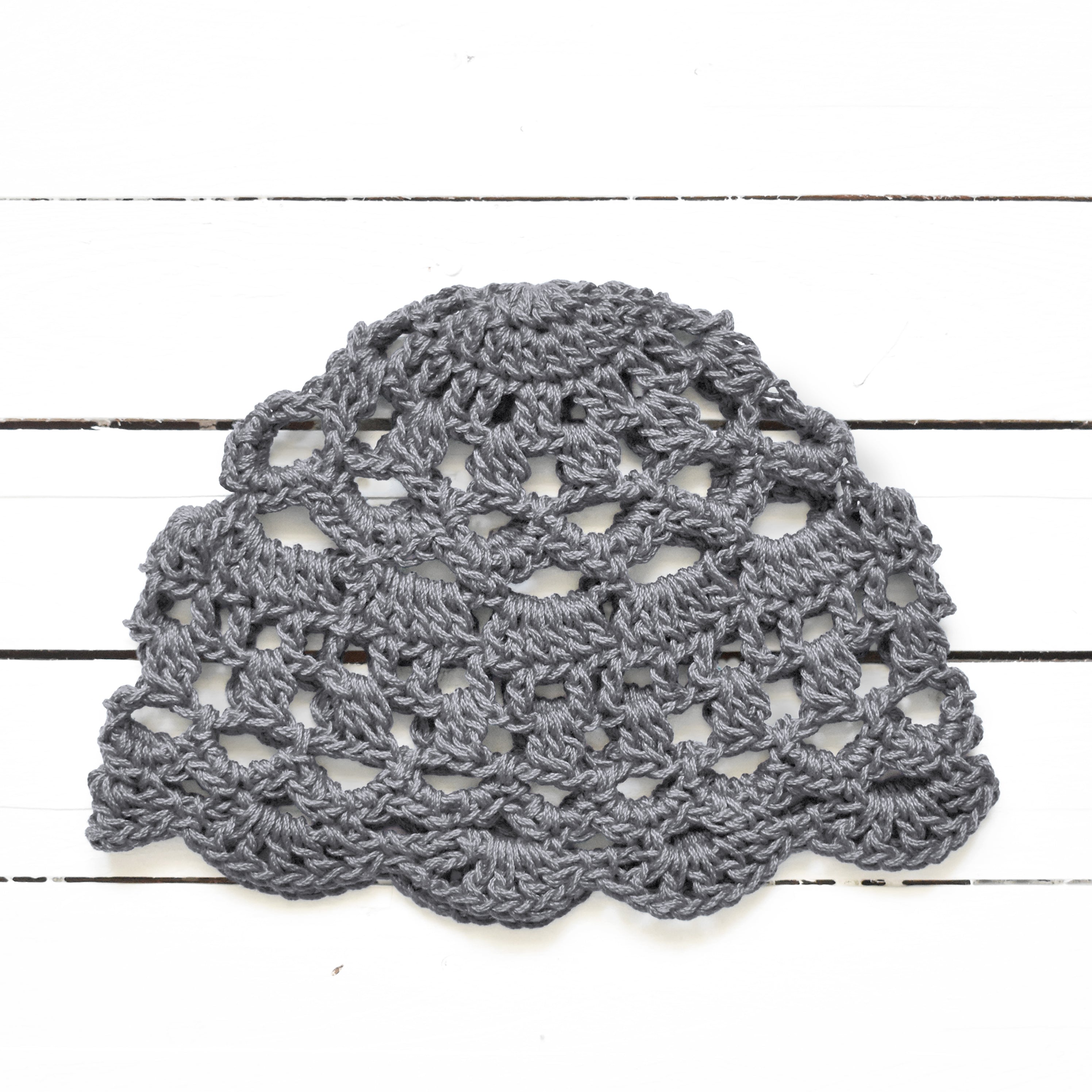 Medium gray crocheted lace summer cap on a white wooden surface.