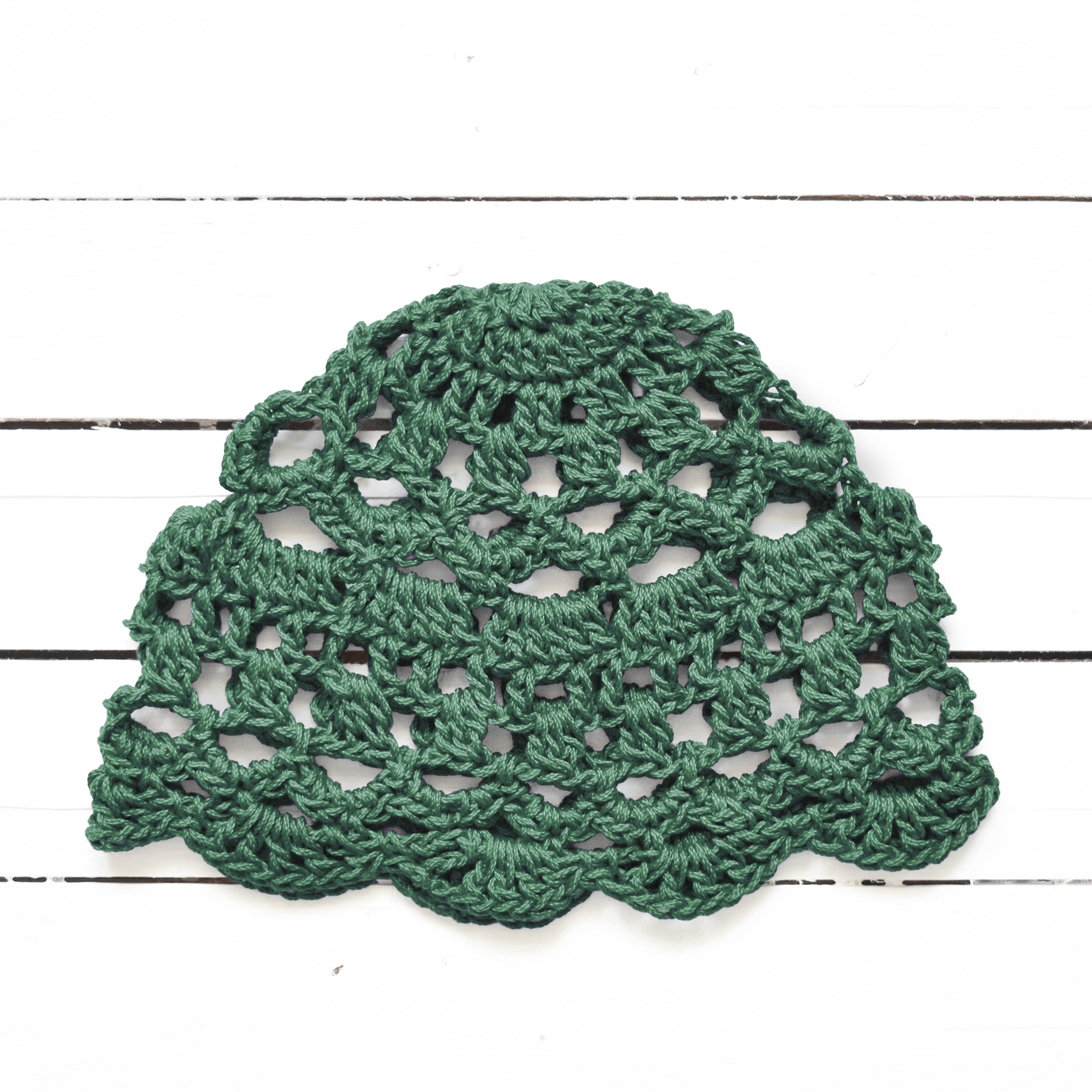 Green crocheted lace skull cap on a white wooden surface.