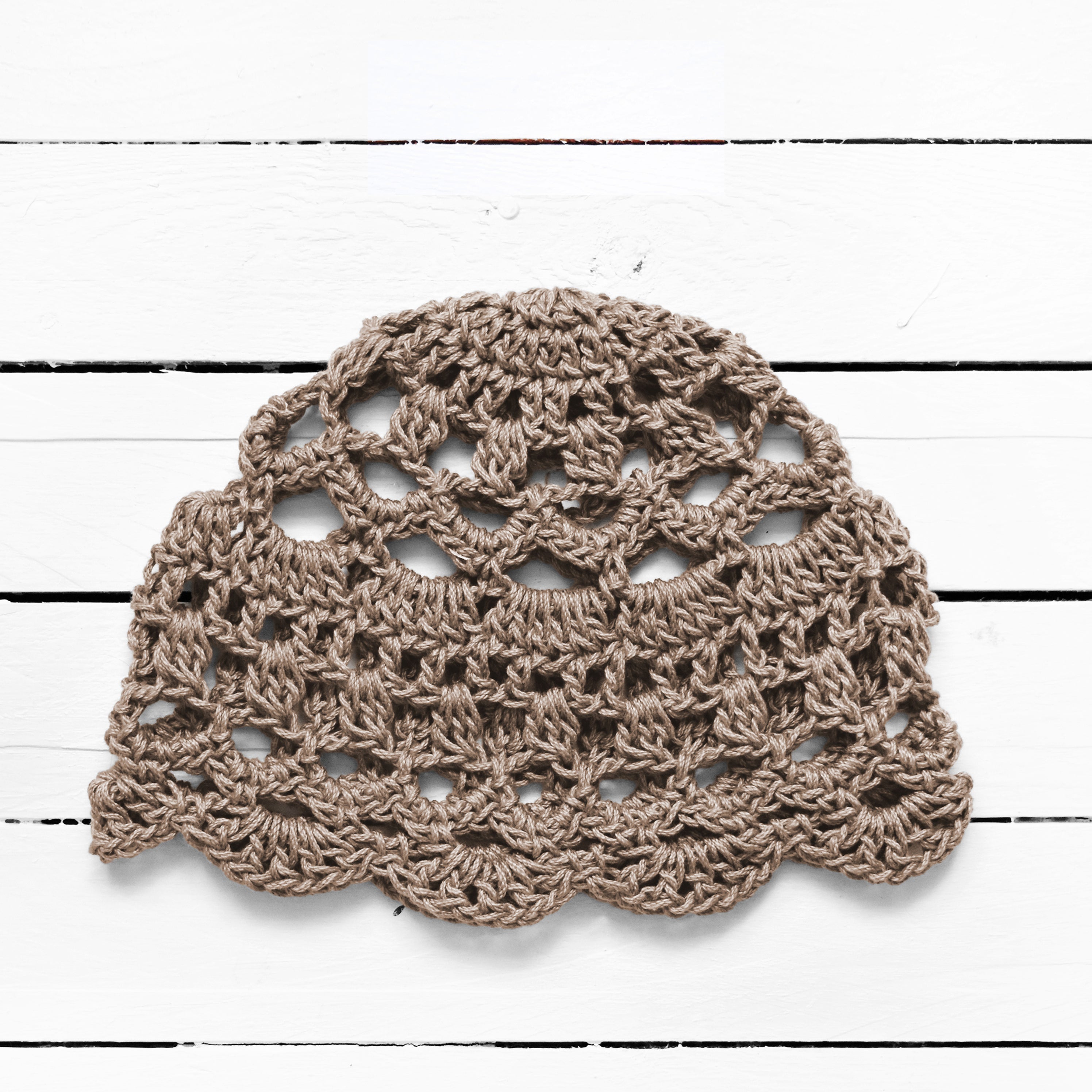 Light brown crocheted lace skull cap on a white wooden surface.
