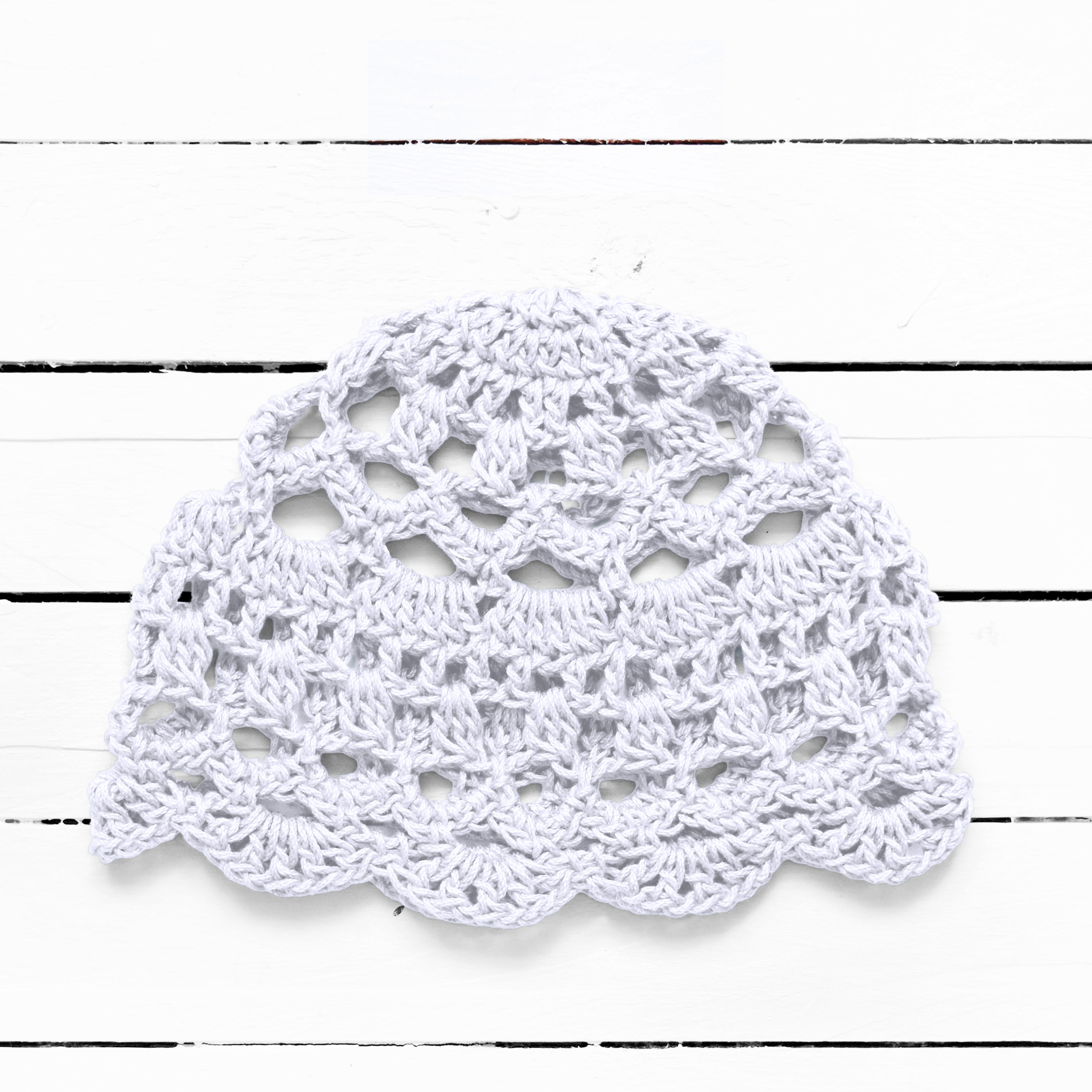 White bohemian lace crocheted summer cap on a white wooden surface.