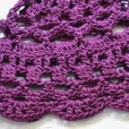 Close-up of a purple crocheted hat with a lace pattern on a light background.