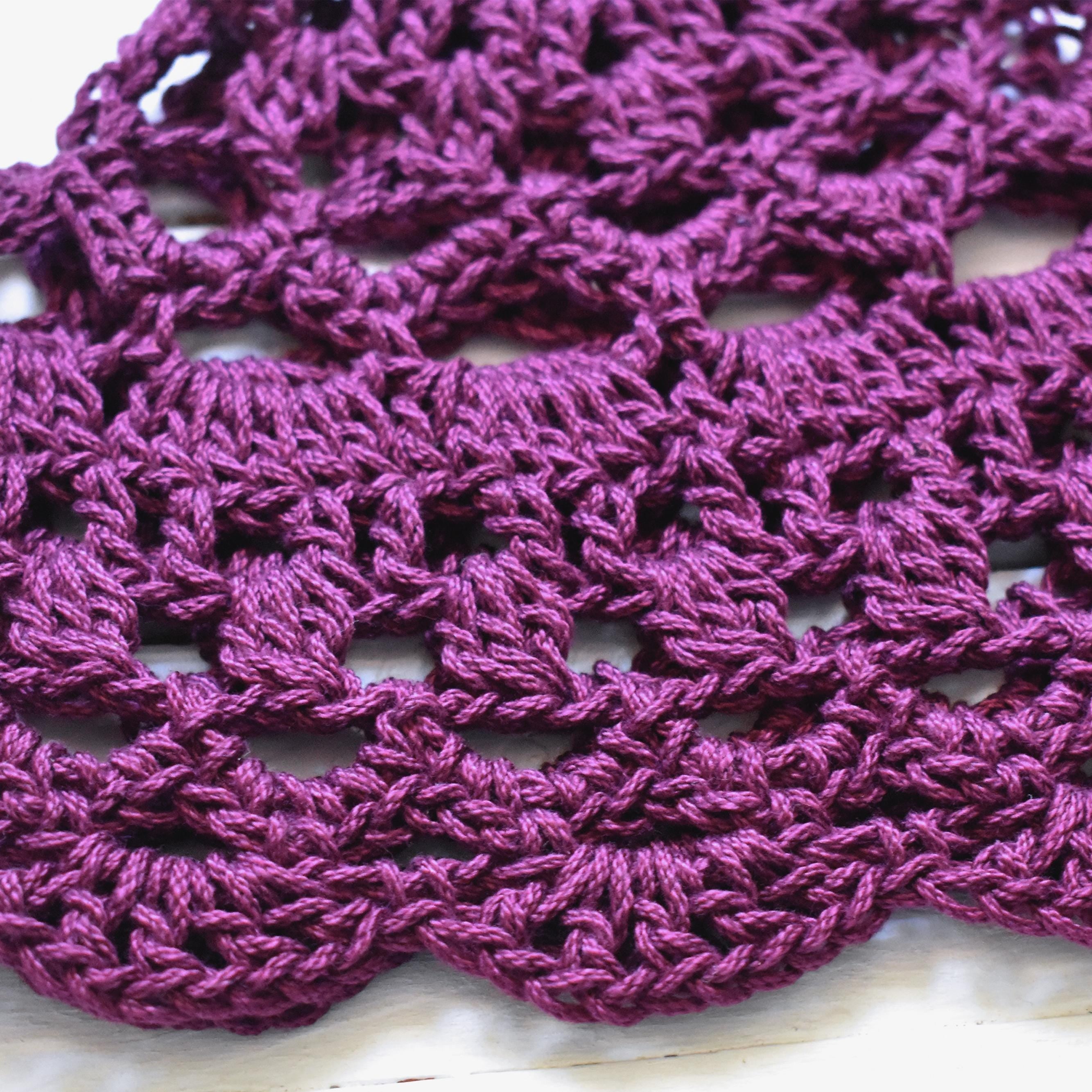 Close-up of a purple crocheted hat with a lace pattern on a light background.