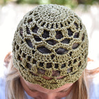 A green lace crochet hat worn by a person with their head tilted downwards in an outdoor setting.