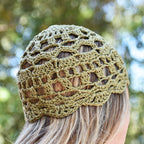 Green crocheted skull cap worn by a person looking into a blurred greenery in the background.