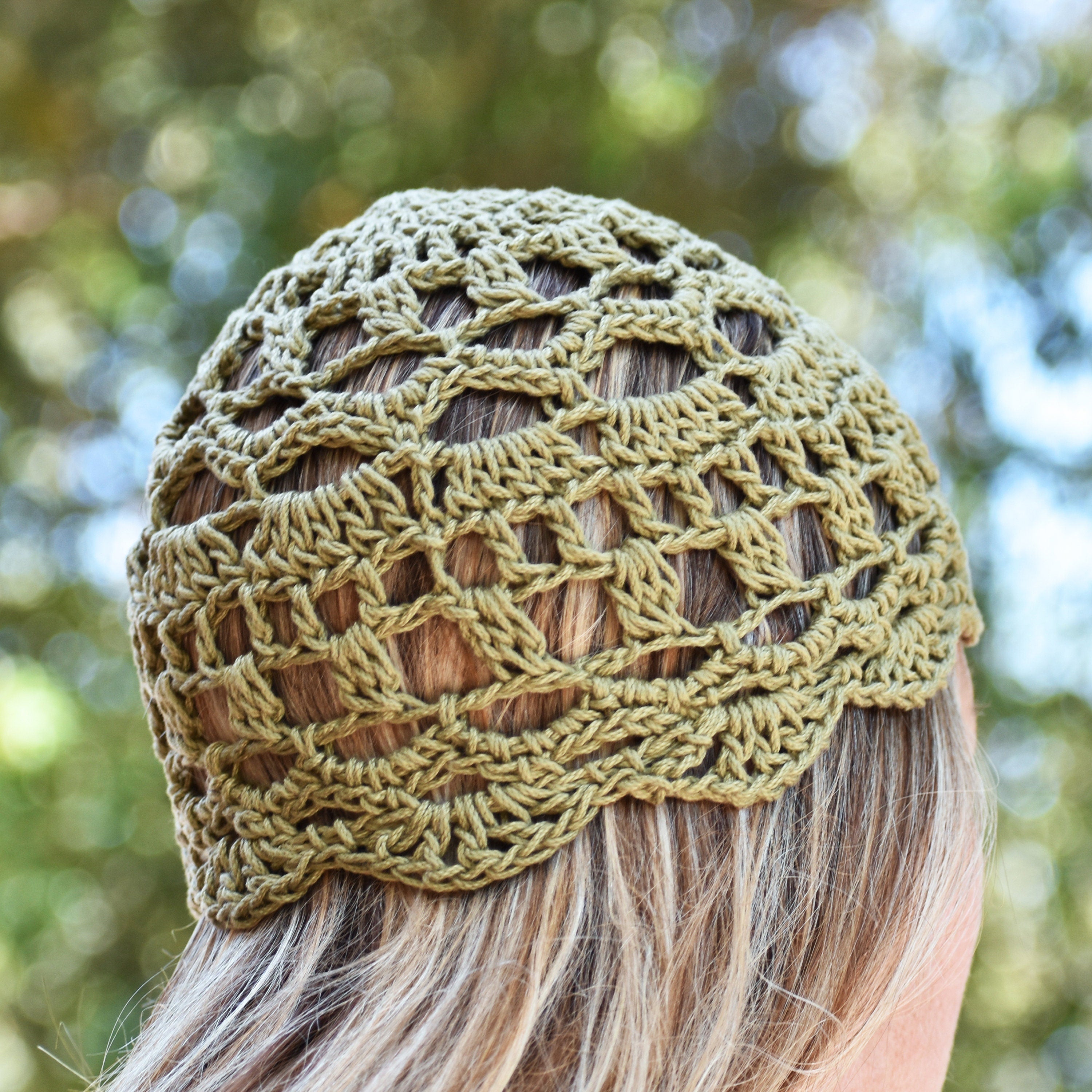 Green crocheted skull cap worn by a person looking into a blurred greenery in the background.