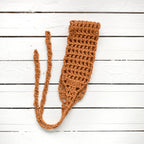 Orange crocheted hair wrap with a long strap on a white wooden surface.