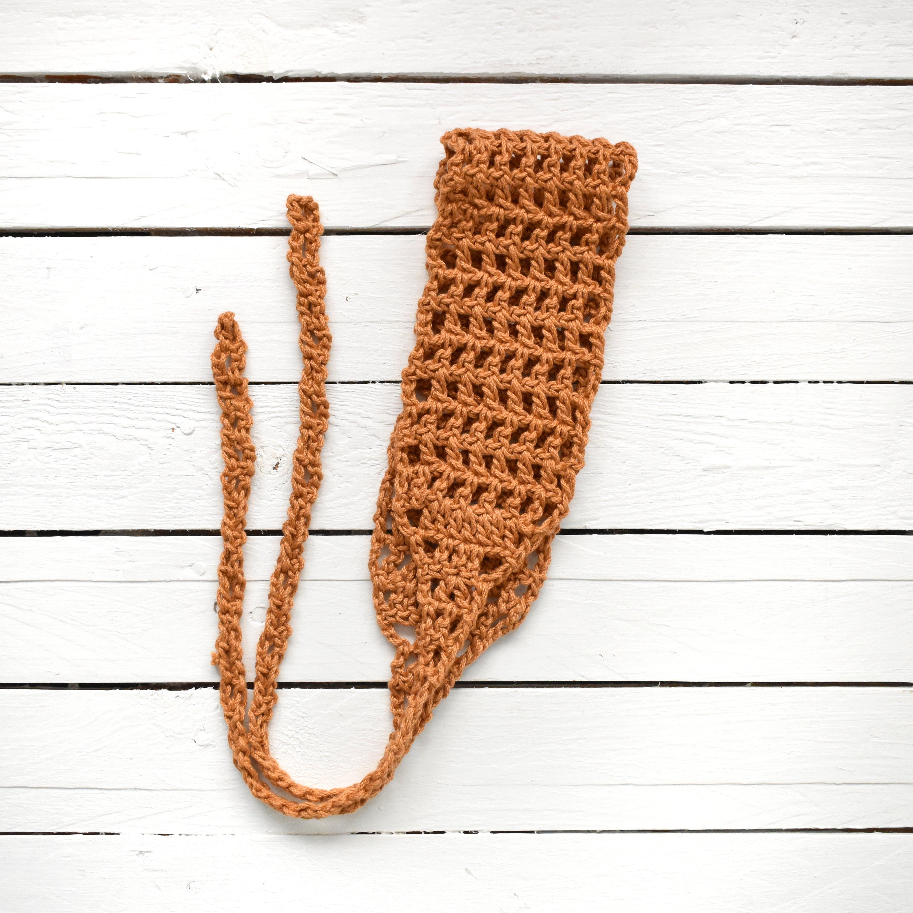 Orange crocheted hair wrap with a long strap on a white wooden surface.