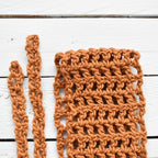 Close-up of an orange crocheted hair wrap on a white wooden surface.