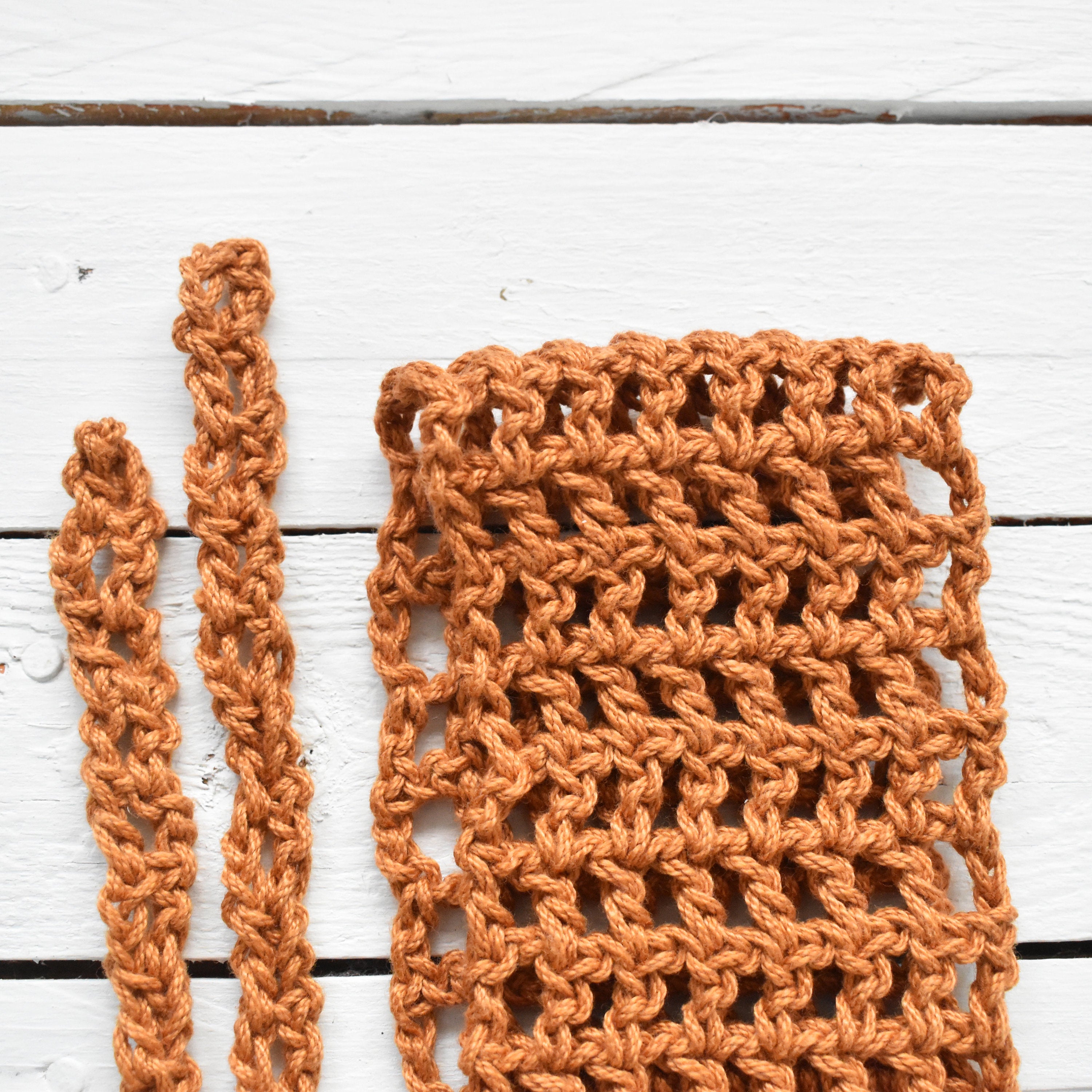 Close-up of an orange crocheted hair wrap on a white wooden surface.