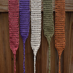 Five crocheted headbands in different colors hanging on a wooden surface.