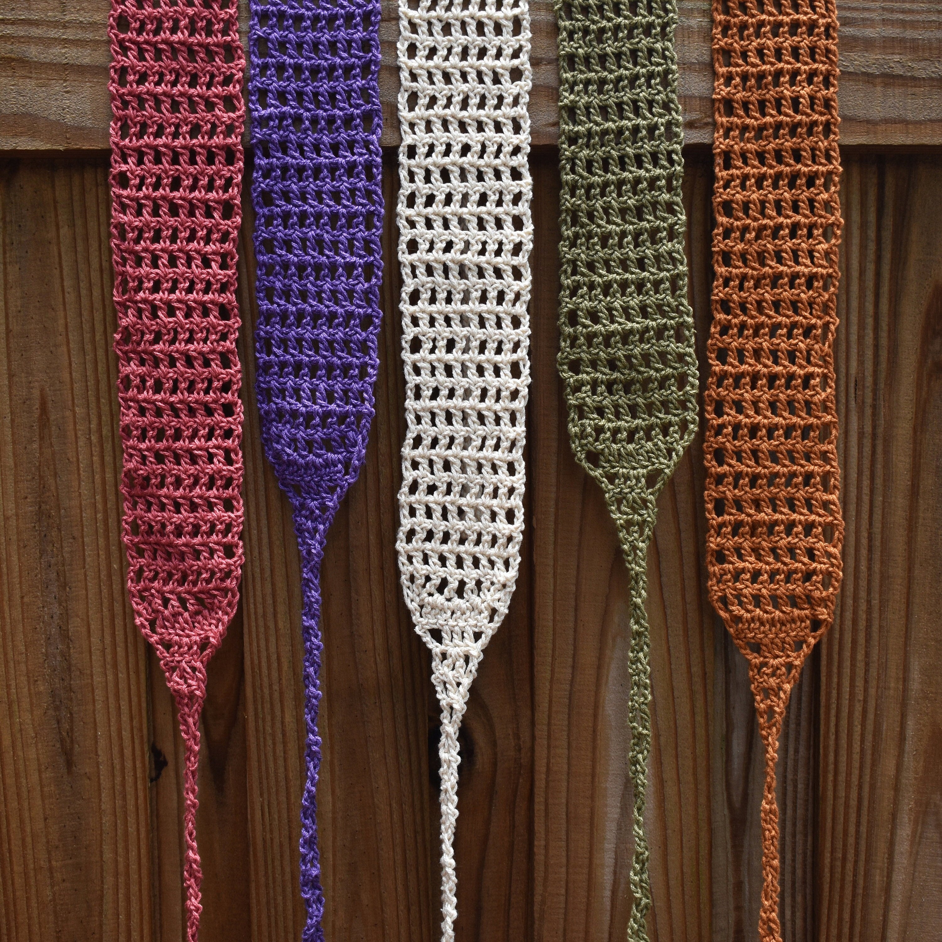 Five crocheted headbands in different colors hanging on a wooden surface.