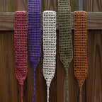 Five crocheted hair wraps in different colors hanging on a wooden surface.