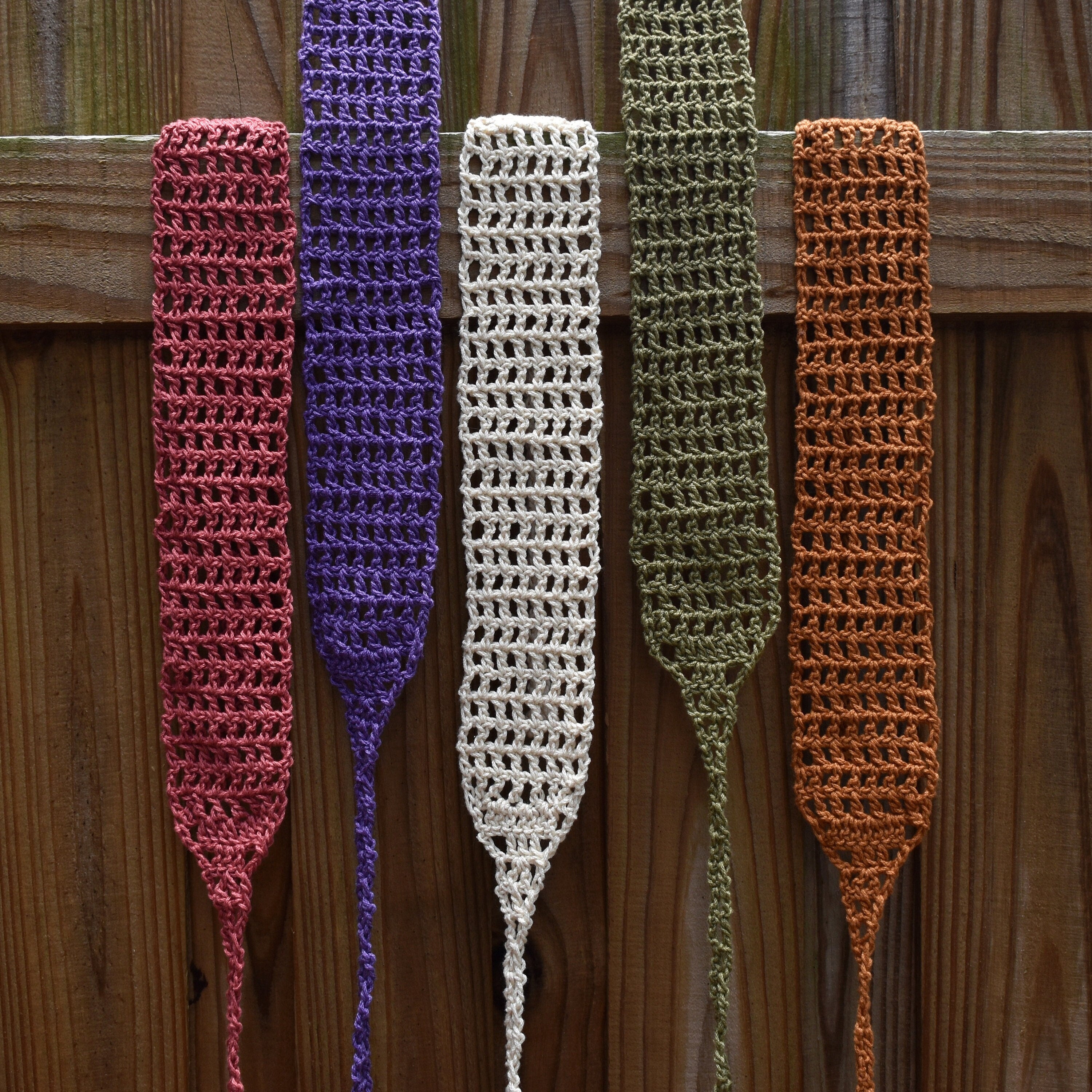 Five crocheted hair wraps in different colors hanging on a wooden surface.
