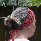 Person wearing a pink knitted headband against a blurred natural background.
