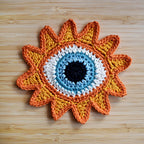 Crocheted sunshine applique with a blue eye in the center on a wooden surface.