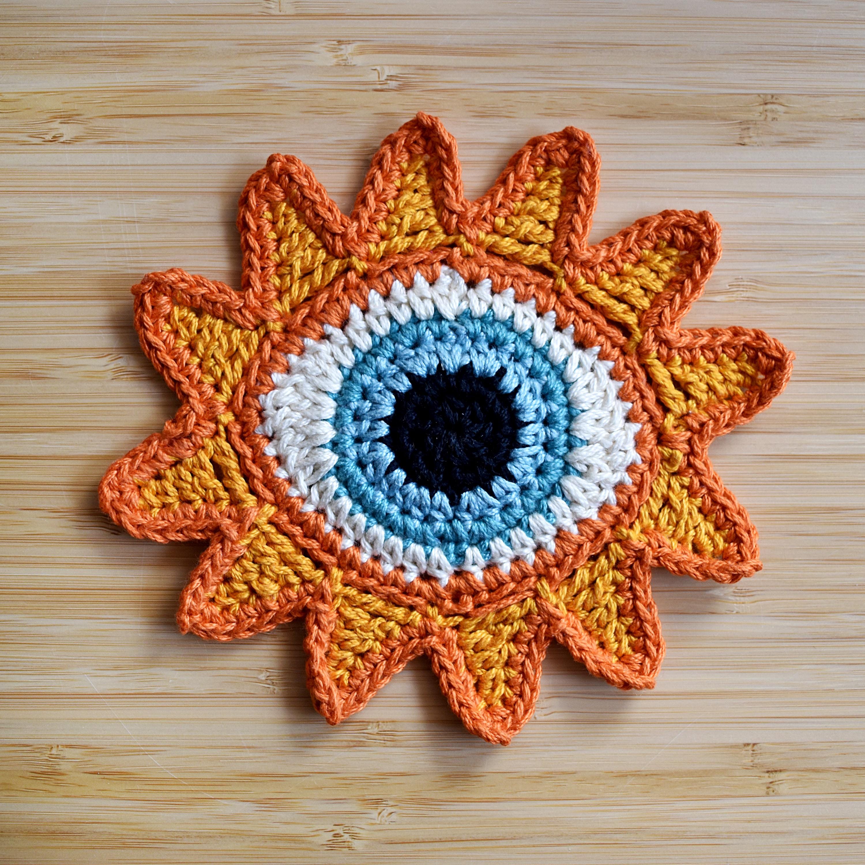 Crocheted sunshine applique with a blue eye in the center on a wooden surface.