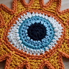 Close-up of a colorful crocheted sun applique with a blue eye in the center.