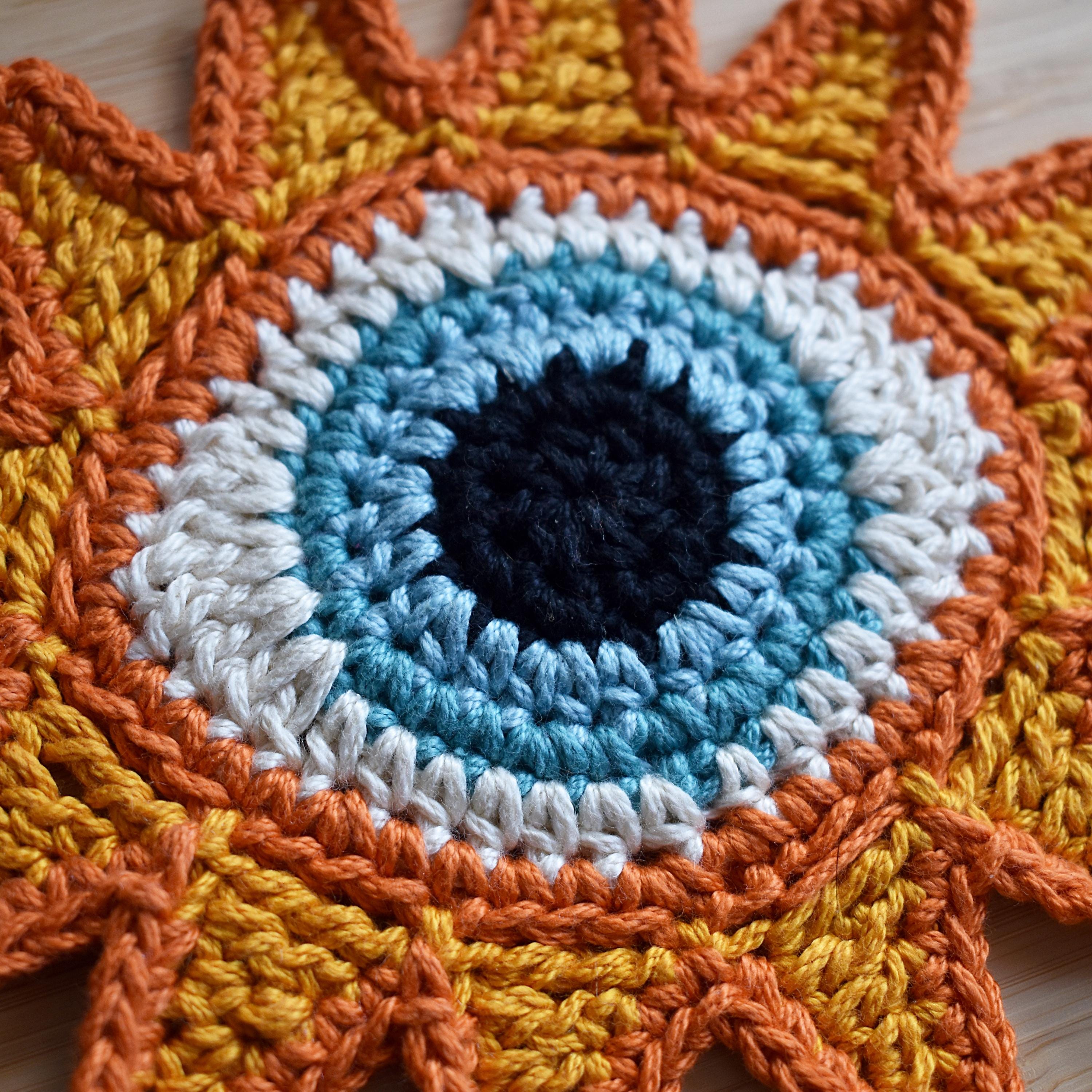 Close-up of a colorful crocheted sun applique with a blue eye in the center.