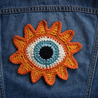 Crocheted sunflower patch with a blue eye in the center on a denim jacket.