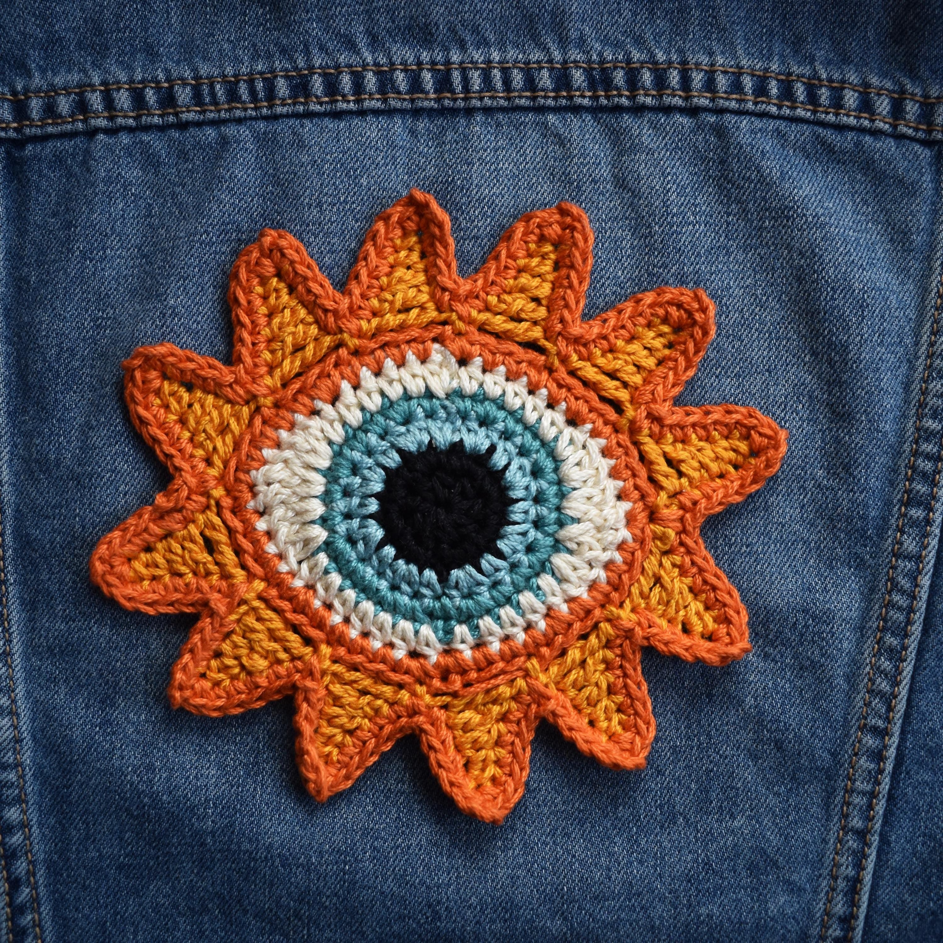 Crocheted sunflower patch with a blue eye in the center on a denim jacket.