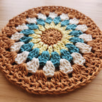 Round crocheted plant mat with a multicolored pattern on a wooden surface.