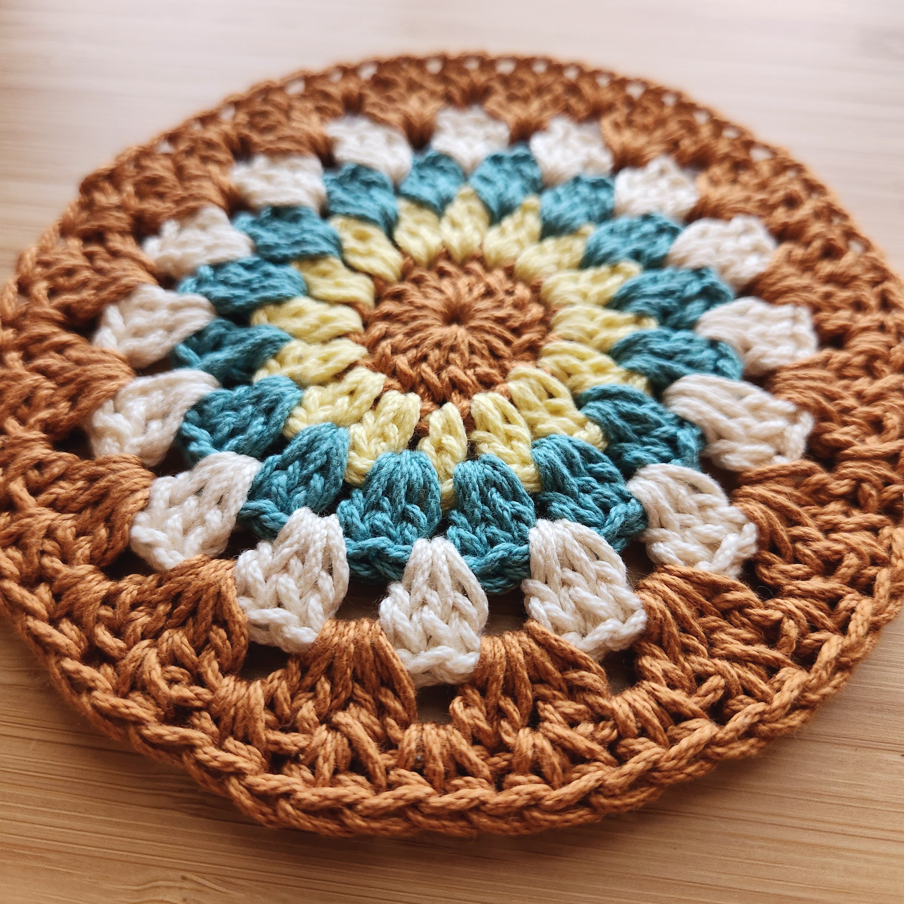 Round crocheted plant mat with a multicolored pattern on a wooden surface.