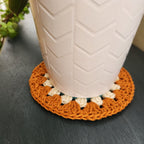 White pot with a white and orange crocheted coaster underneath on a dark blue surface.