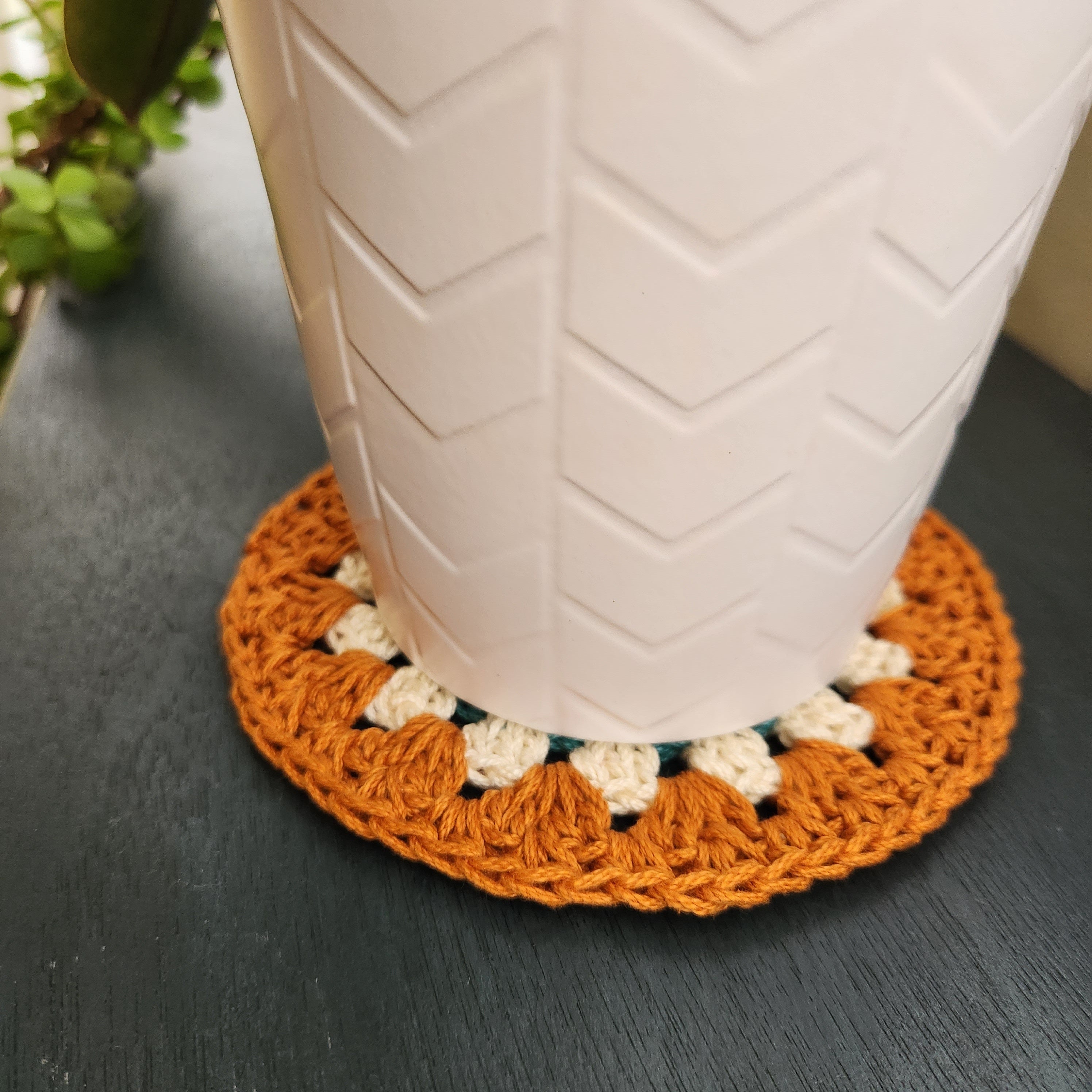 White pot with a white and orange crocheted coaster underneath on a dark blue surface.