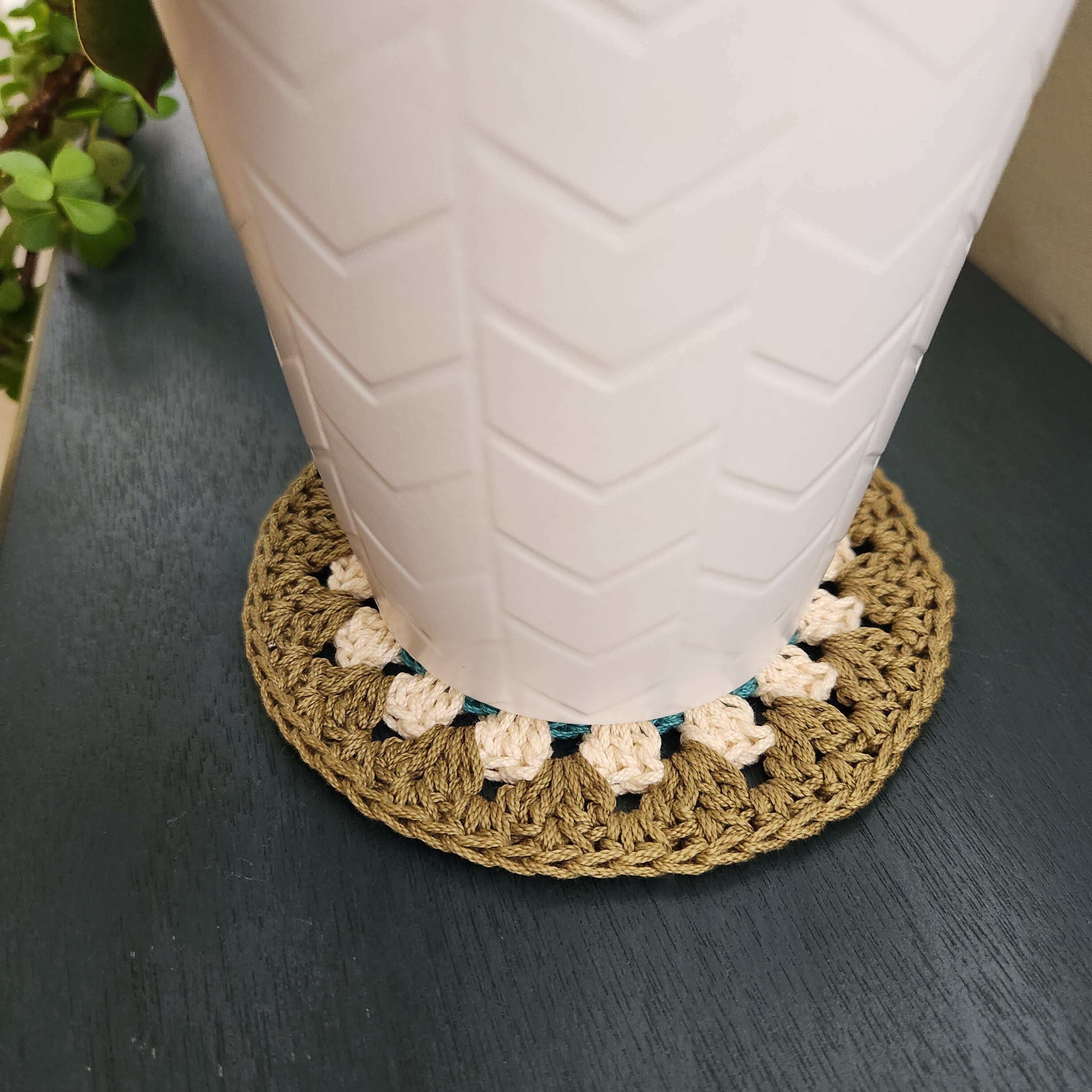 White textured vase on a dark surface with a crocheted coaster featuring floral patterns.