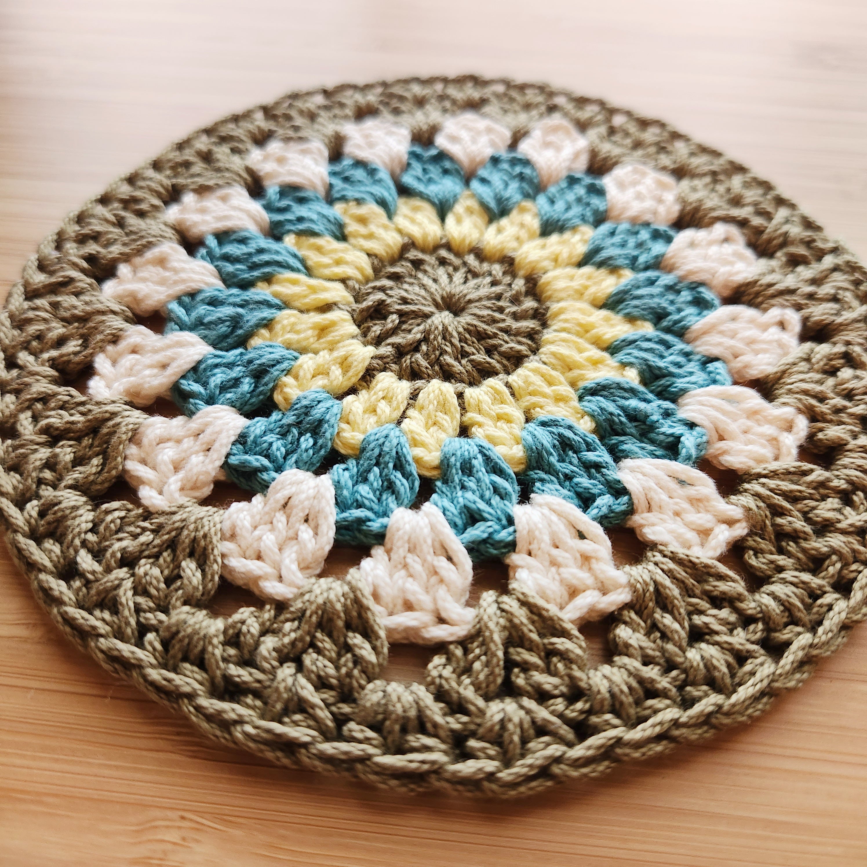 Crocheted round mat with multicolor pattern on a wooden surface.