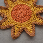 Crocheted sunshine appliqué with orange and yellow colors on a natural kraft background.