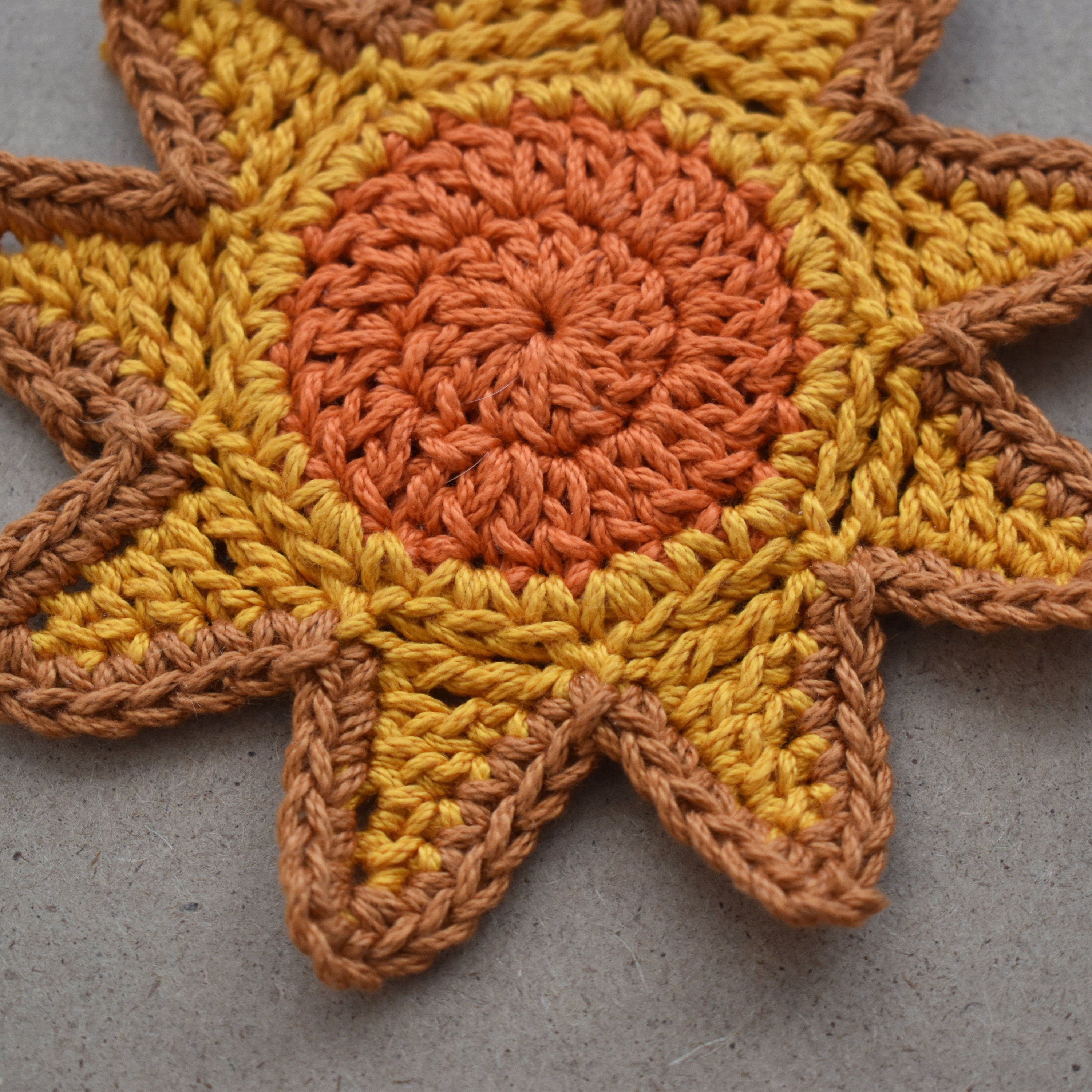 Crocheted sunshine appliqué with orange and yellow colors on a natural kraft background.