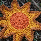 Crocheted sunshine applique with orange and yellow colors on a grassy background.