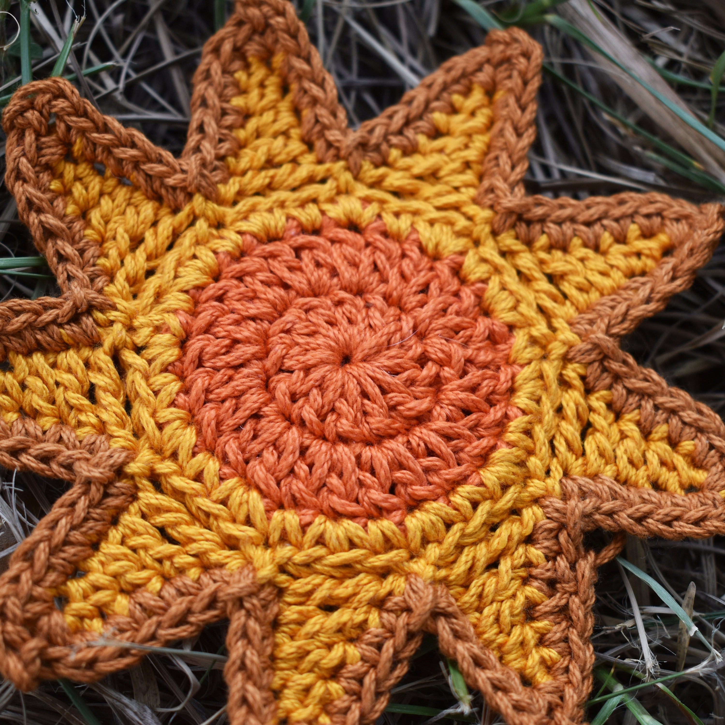 Crocheted sunshine applique with orange and yellow colors on a grassy background.