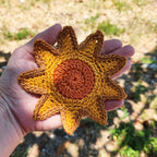 Hand holding a crocheted sunflower with a blurred natural background.