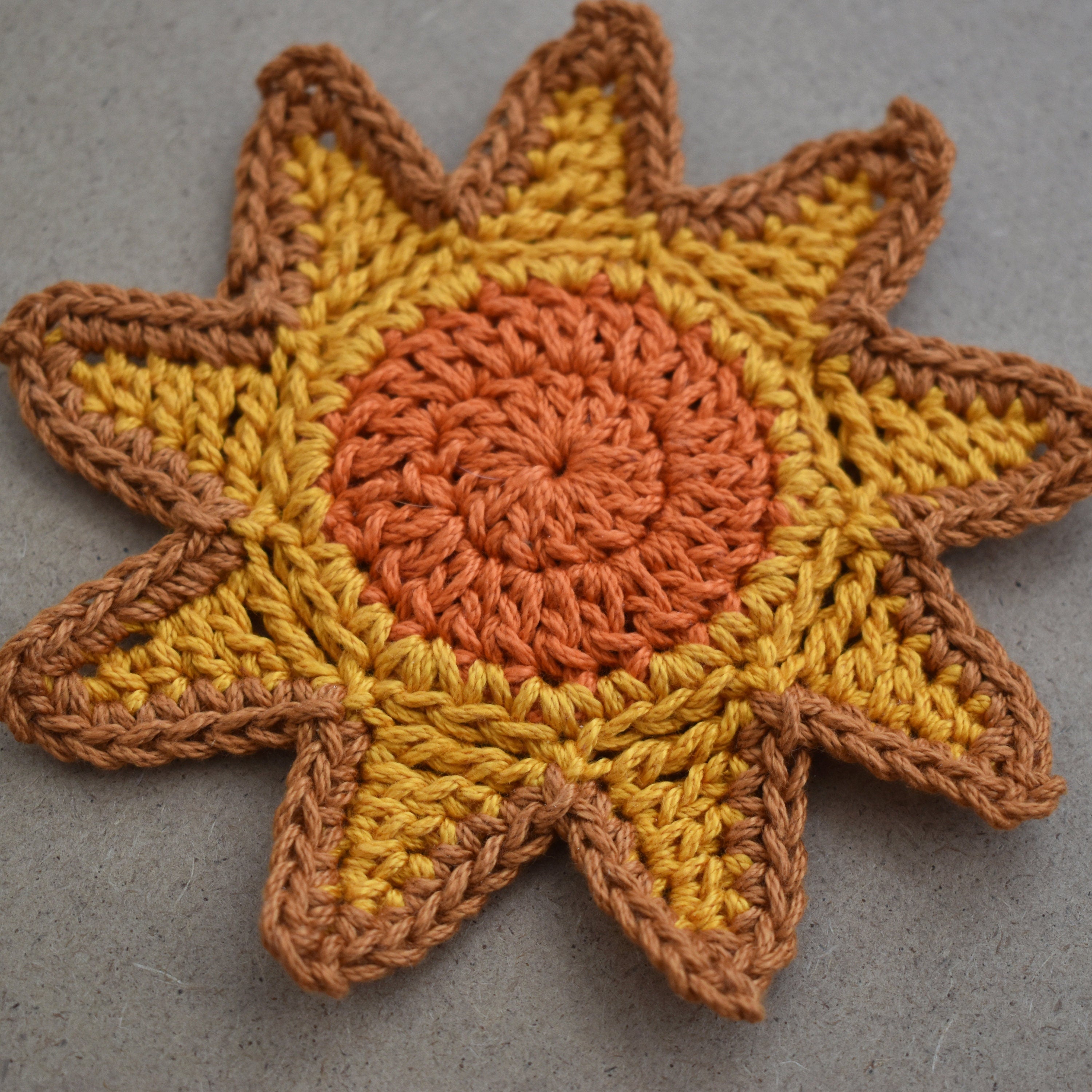 Crocheted sunshine motif with orange and yellow colors on a kraft textured background.