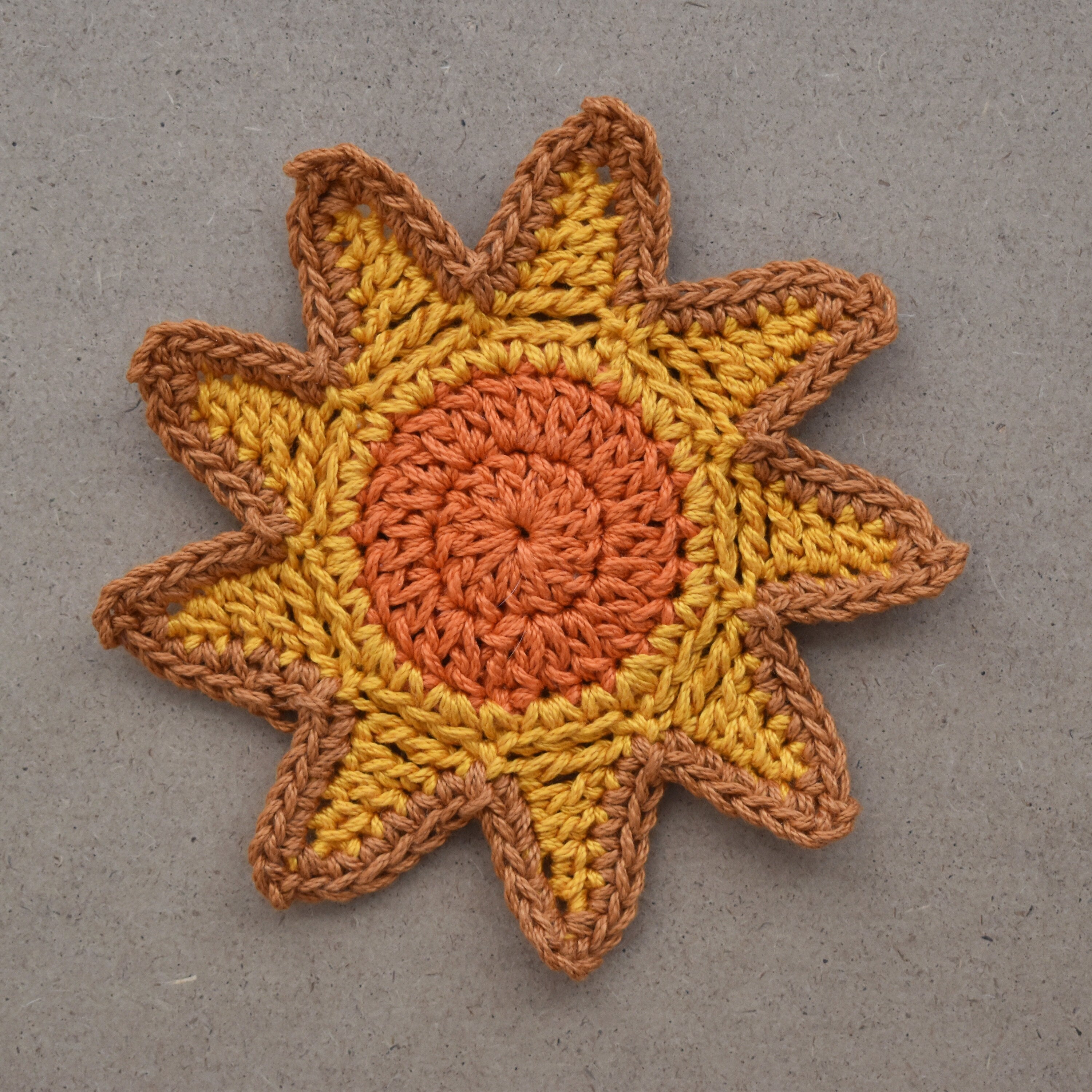 Crocheted sunshine applique with orange and yellow colors on a natural kraft background.