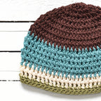 Crocheted beanie with brown, blue, beige, and green colors on a white wooden surface.