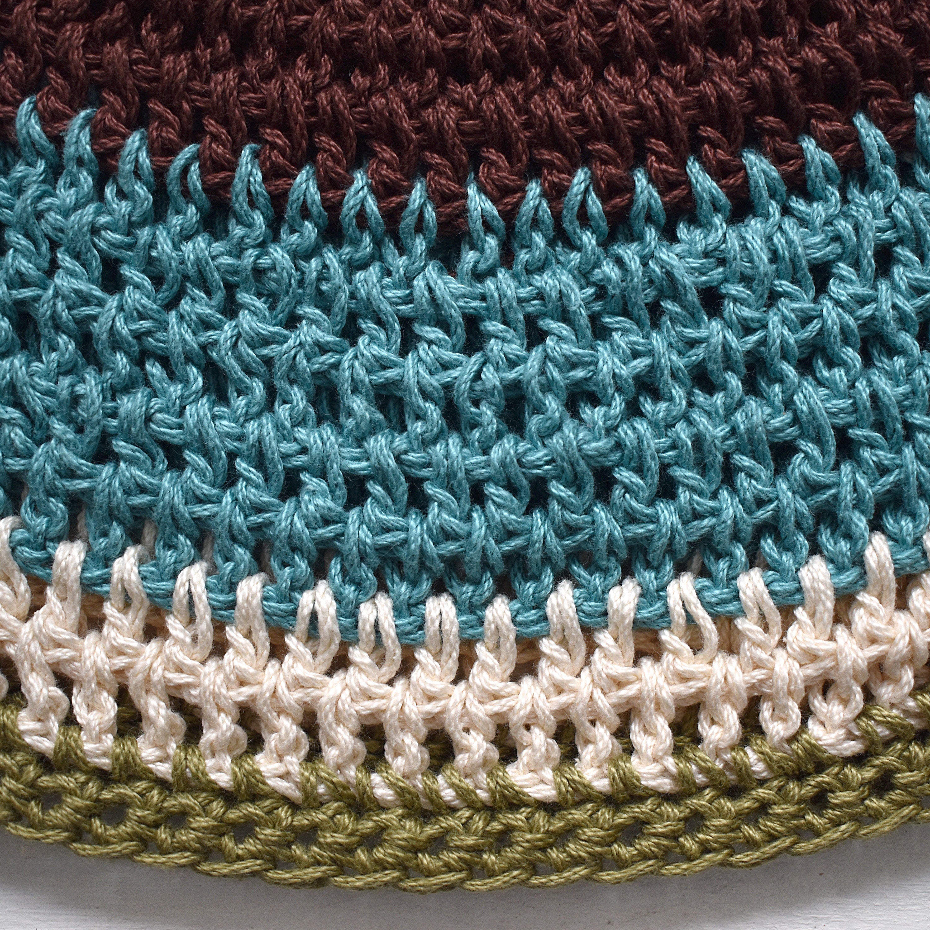 Close-up of a crocheted hat with a multicolored striped pattern on a white background.