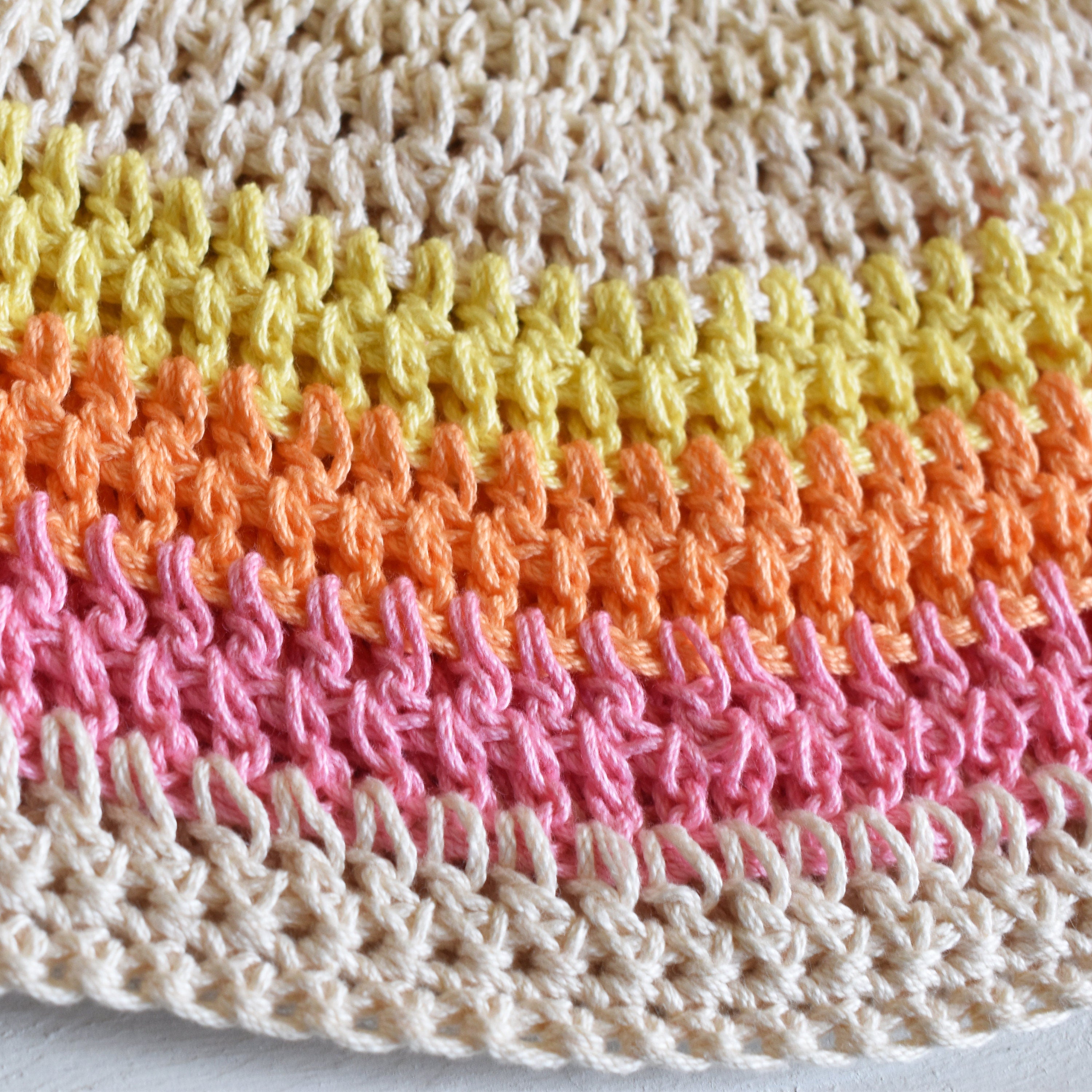 Close-up of a colorful crocheted hat with beige, yellow, orange, and pink stripes on a light background.