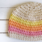 Colorful striped knitted beanie on a white wooden surface.