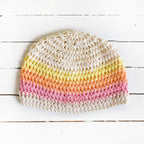 Beige knitted beanie with colorful stripes on a white wooden surface.