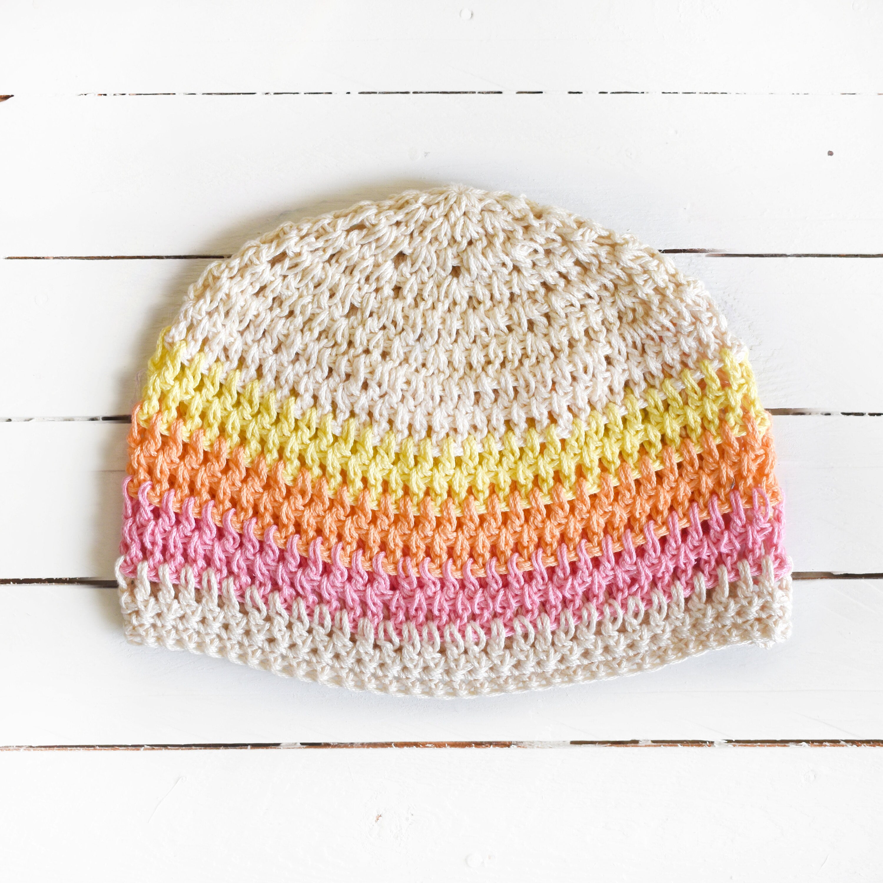 Beige knitted beanie with colorful stripes on a white wooden surface.
